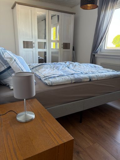 Schlafzimmer mit Bett, Holztischlampe und Kleiderschrank im Hintergrund.