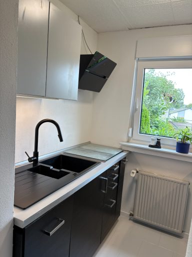 Moderne Küche mit schwarzen Schränken, Spüle und Fensterblick ins Freie.