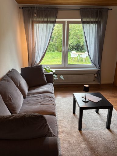 Gemütliches Wohnzimmer mit Sofa, Tisch und Blick auf den Garten.